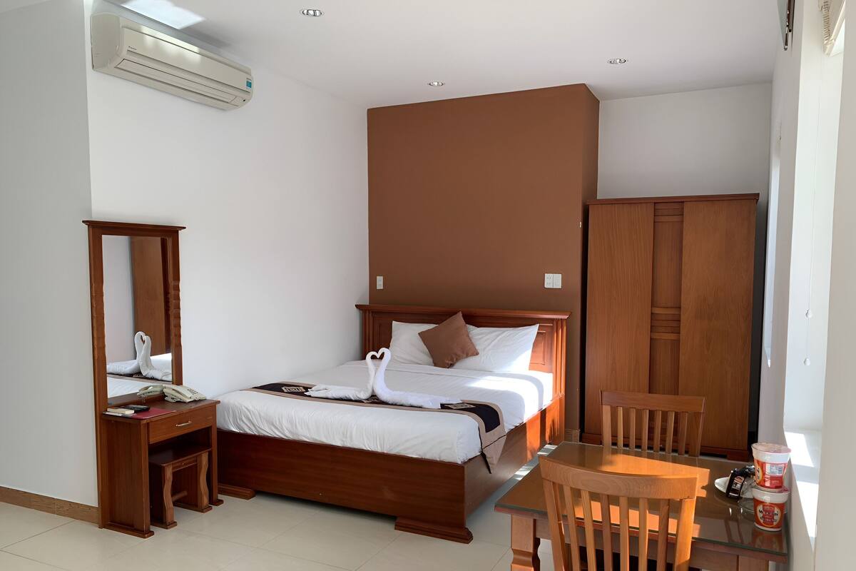 A hotel room with a wooden bed, a wooden desk with a telephone, a mirror, and a wooden wardrobe.