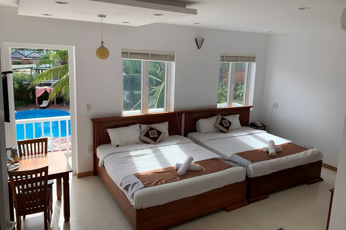 A hotel room with two beds, a dining table, and a view of a swimming pool.