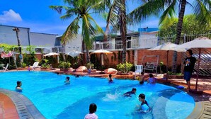 A swimming pool with multiple people in the water, surrounded by palm trees and lounge chairs. - Volga Hotel Mui Ne (Mui Ne)