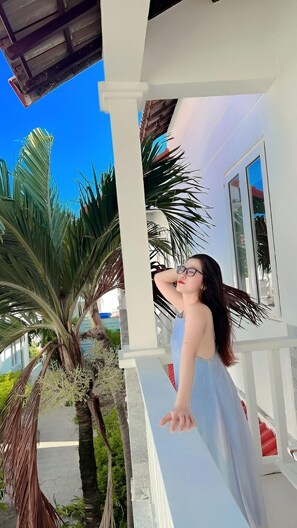 A person standing on a white porch with a view of palm trees and a clear blue sky. - Volga Hotel Mui Ne (Mui Ne)