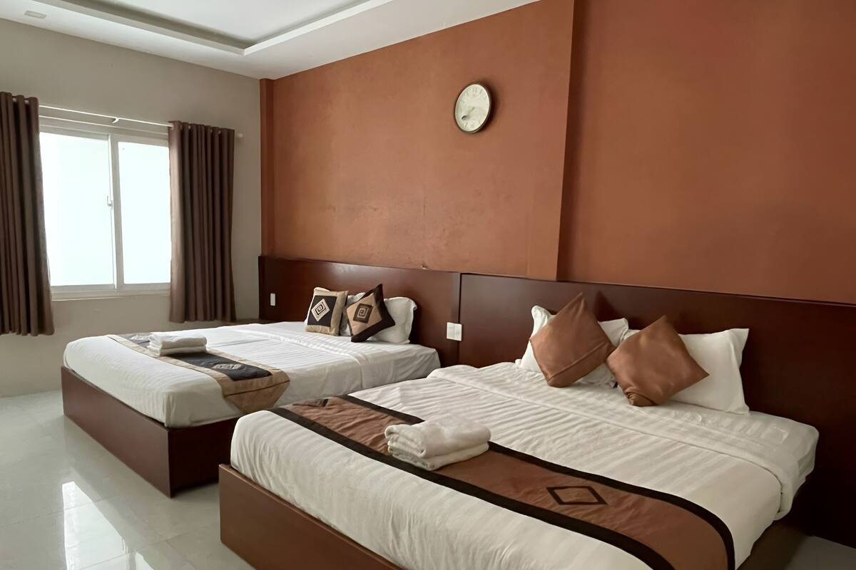 A modern hotel room with two beds, a large window, and a clock on the wall.