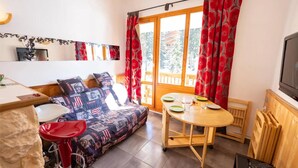 A cozy room with a sofa, a dining table, and a TV. - Mezzanine Studio 'Le Thabor' with Mountain View and Balcony (Modane)