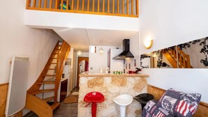 A kitchen with a stone island, wooden staircase, and a high ceiling. - Mezzanine Studio 'Le Thabor' with Mountain View and Balcony (Modane)