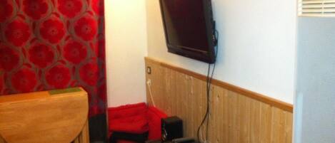 A room with a television mounted on the wall, a wooden cabinet, and a red chair.