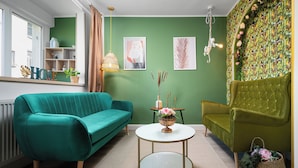 A room with a teal sofa, a green armchair, a round white table, and a green patterned wall. - Amazon Apartment - Cismigiu Gardens for 2 guests (București)