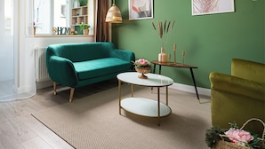 A living room with a teal sofa, a round coffee table, and a green armchair. There are two paintings on the wall, a window with curtains, and a shelf with decorative items. - Amazon Apartment - Cismigiu Gardens for 2 guests (București)