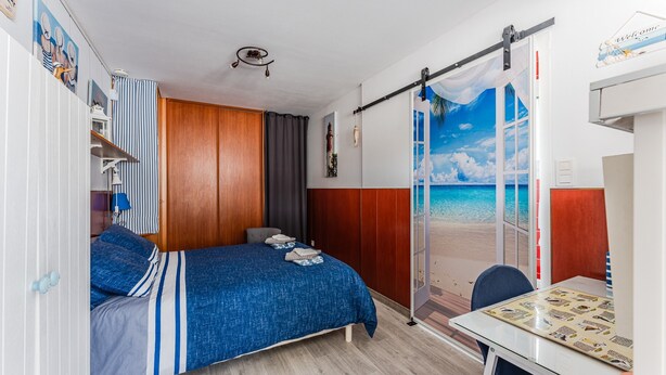 A bedroom with a bed, a desk, and a sliding door to a balcony. - Chez Brigitte – Charming Studio in Audenge with Terrace, Bikes, and Close to Bassin d'Arcachon (Audenge)