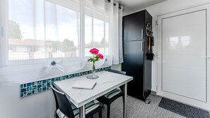 A compact kitchen with a dining area, a refrigerator, and a view through the window. - Chez Brigitte – Charming Studio in Audenge with Terrace, Bikes, and Close to Bassin d'Arcachon (Audenge)