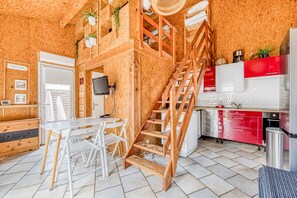 Una cocina con paredes de madera, una escalera, un comedor con mesa y sillas, y un electrodoméstico rojo.