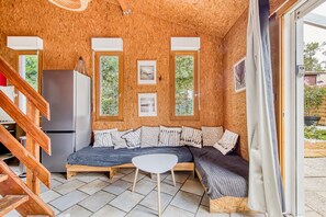 A cozy room with a wooden ceiling, a sofa, a small table, and a refrigerator.