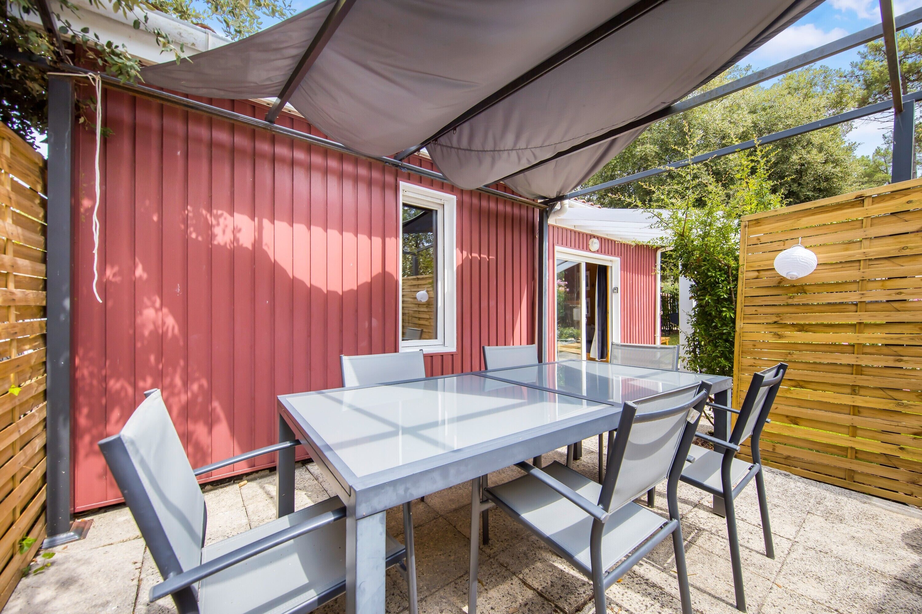 A red building with a glass table and chairs, a wooden fence, and a covered area.
