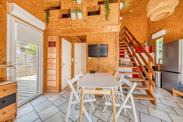 A wooden interior with a dining table, chairs, a TV, and a staircase.