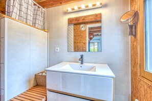 Un baño con lavamanos blanco, tocador de madera, un espejo con iluminación y una ventana con vistas.