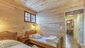 A wooden-paneled room with two beds, a nightstand, a lamp, and a window.
