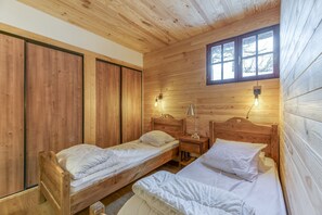 Een houten kamer met twee eenpersoonsbedden, een nachtkastje met een lamp en een raam.