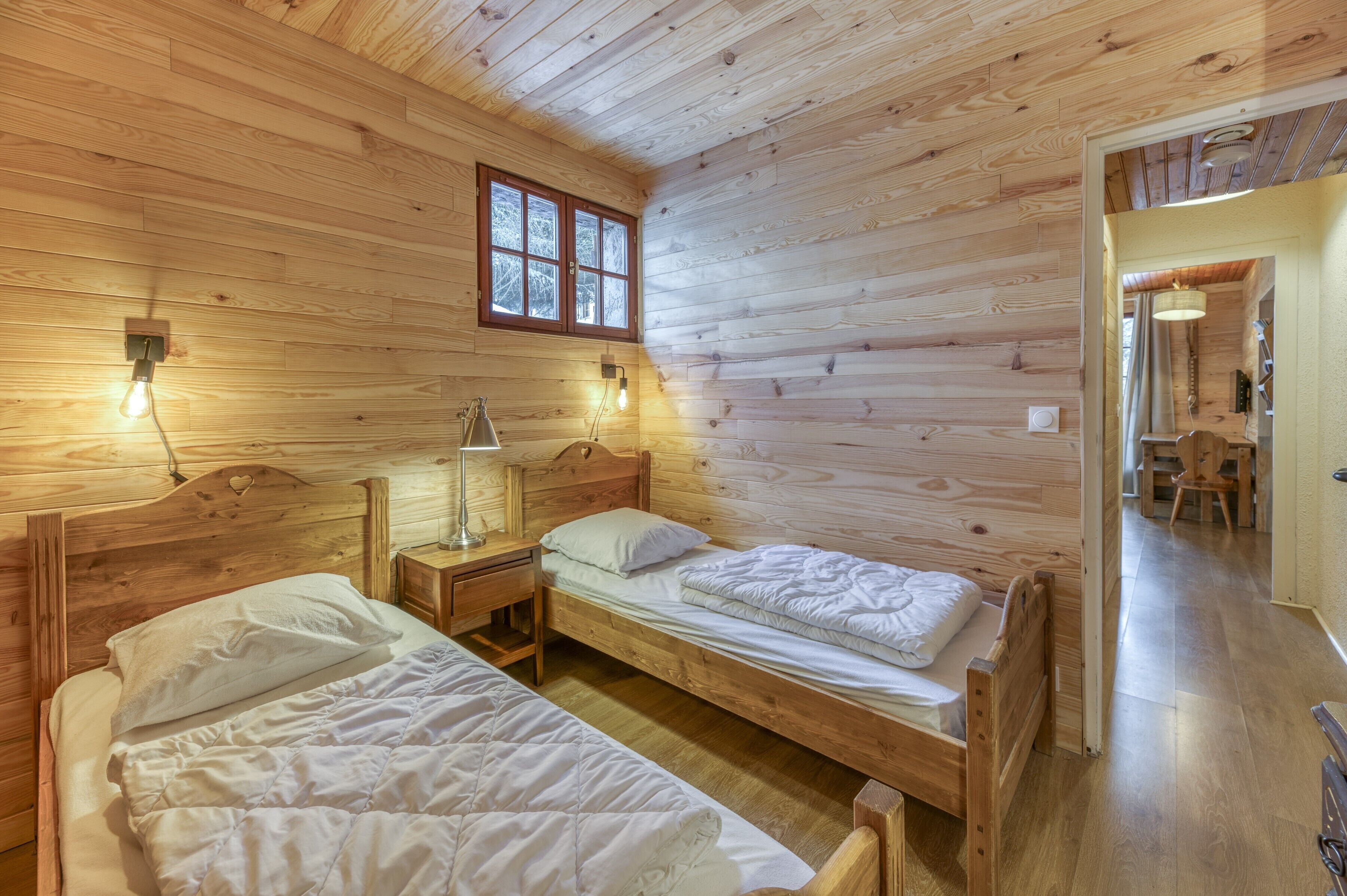 Une chambre dans un chalet en bois, avec deux lits, une fenêtre et une table de chevet avec une lampe.