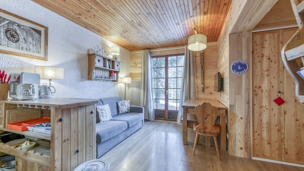 A cozy cabin interior with a wooden ceiling, a sofa, a dining table, and a kitchen area.