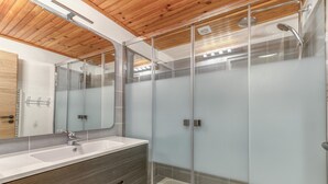 A modern bathroom with a glass-enclosed shower, a wooden ceiling, and a large mirror.