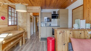 Een houten interieur met een keuken, een eethoek en een rode prullenbak.