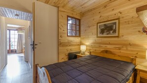 Een kamer met houten lambrisering, een bed, een nachtkastje, een lamp, een lijst met een afbeelding en een raam.