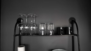 A black metal shelf with wine glasses, a roll of toilet paper, and a bowl.
