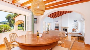 A dining area with a round wooden table, wicker chairs, and a hanging light fixture. - Holiday Home 'Aladern' with Sea View, Private Terrace and Wi-Fi (Font de Sa Cala)
