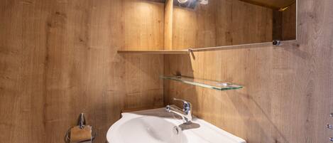 A wooden wall with a white sink, a glass shelf, and two ceiling lights.