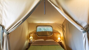 Een tent met een bed, twee nachtkastjes met lampen en een raam met uitzicht.