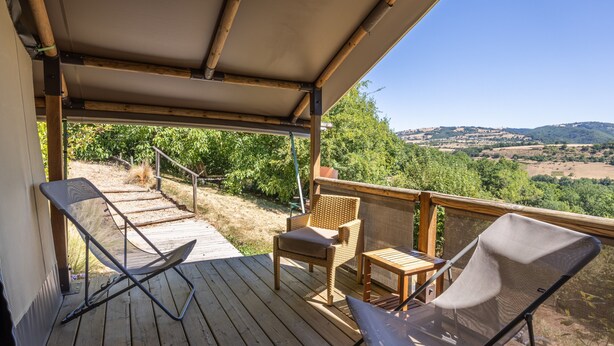 Een houten terras met twee stoelen en een tafel, met uitzicht op een landschap met bomen en heuvels.
