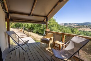 Een houten terras met twee stoelen en een tafel, met uitzicht op een landschap met bomen en heuvels.