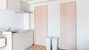 A modern kitchen with wooden cabinets, a stainless steel sink, and a built-in range hood. There are two white trash bins and two wooden doors.