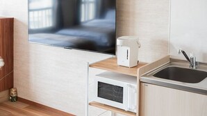 A modern kitchen with a flat-screen TV mounted on the wall, a coffee maker, a microwave, and a sink.