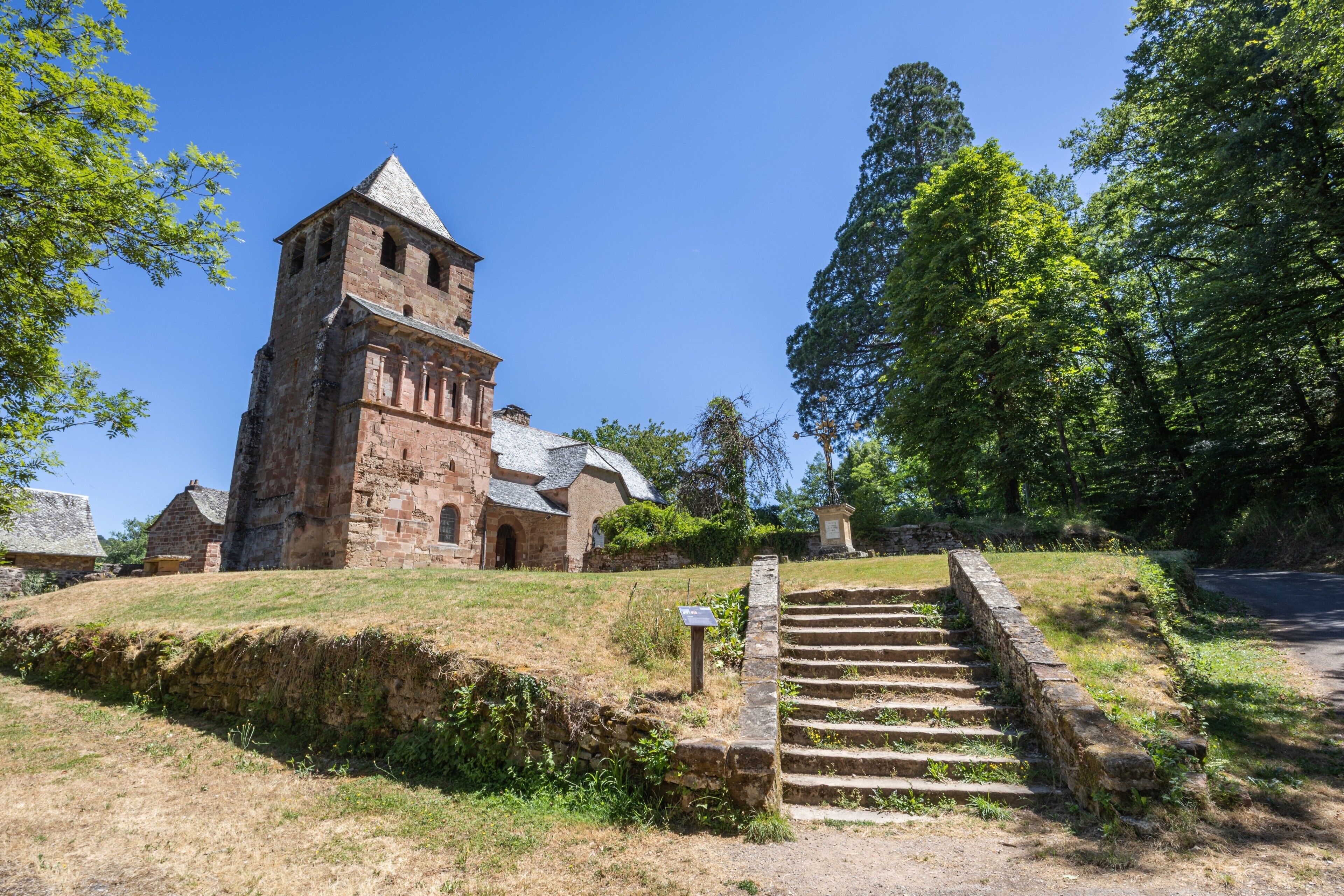 Un bâtiment historique en pierre, doté d’un clocher, d’un escalier en pierre et d’un chemin menant à l’entrée.