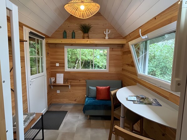 A cozy cabin room with a wooden interior, a window with a view of greenery, a small table, and a bench.