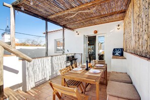 Un espace extérieur abrité, aménagé pour les repas, avec une table pour quatre personnes, des chaises en bois et une pergola au-dessus.