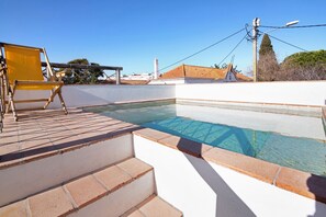 Une piscine sur le toit, avec des marches menant à l’eau, une chaise jaune et un ciel bleu azur.