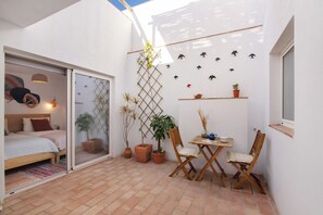 Une petite pièce bien éclairée, avec un lit, une table entourée de chaises et des plantes en pot.