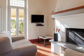 Un salon comprenant un canapé, un téléviseur fixé au mur, une cheminée et une fenêtre donnant sur un paysage verdoyant.