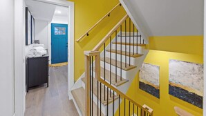 Un escalier avec des marches en bois et des rampes noires, menant à une pièce dotée d’une porte bleue et d’un meuble noir contenant des serviettes.