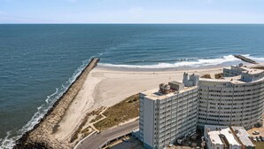 Un hôtel situé sur la côte, avec vue sur la plage, un parking et une architecture aux lignes courbes.