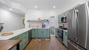 Une cuisine moderne avec des armoires de couleur turquoise, un réfrigérateur en acier inoxydable et un plan de travail en bois.