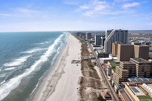 Paisagem costeira com praia, edifícios altos e céu limpo.