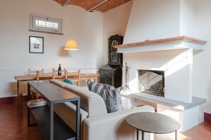A cozy living room with a fireplace, a wooden table, a sofa, and a lamp. - Apartment 'Magazzino 2 Classic' with Shared Pool, Wi-Fi and Air Conditioning (Cortona)
