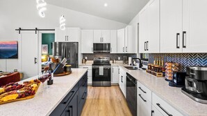 A modern kitchen with white cabinets, stainless steel appliances, and a central island with a wine glass and grapes.