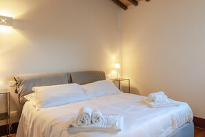 A neatly made bed with white linens and rolled towels, a bedside lamp, and a nightstand with a lamp. - Holiday Home 'Frantoio 4 Superior' with Shared Pool, Wi-Fi and Air Conditioning (Cortona)
