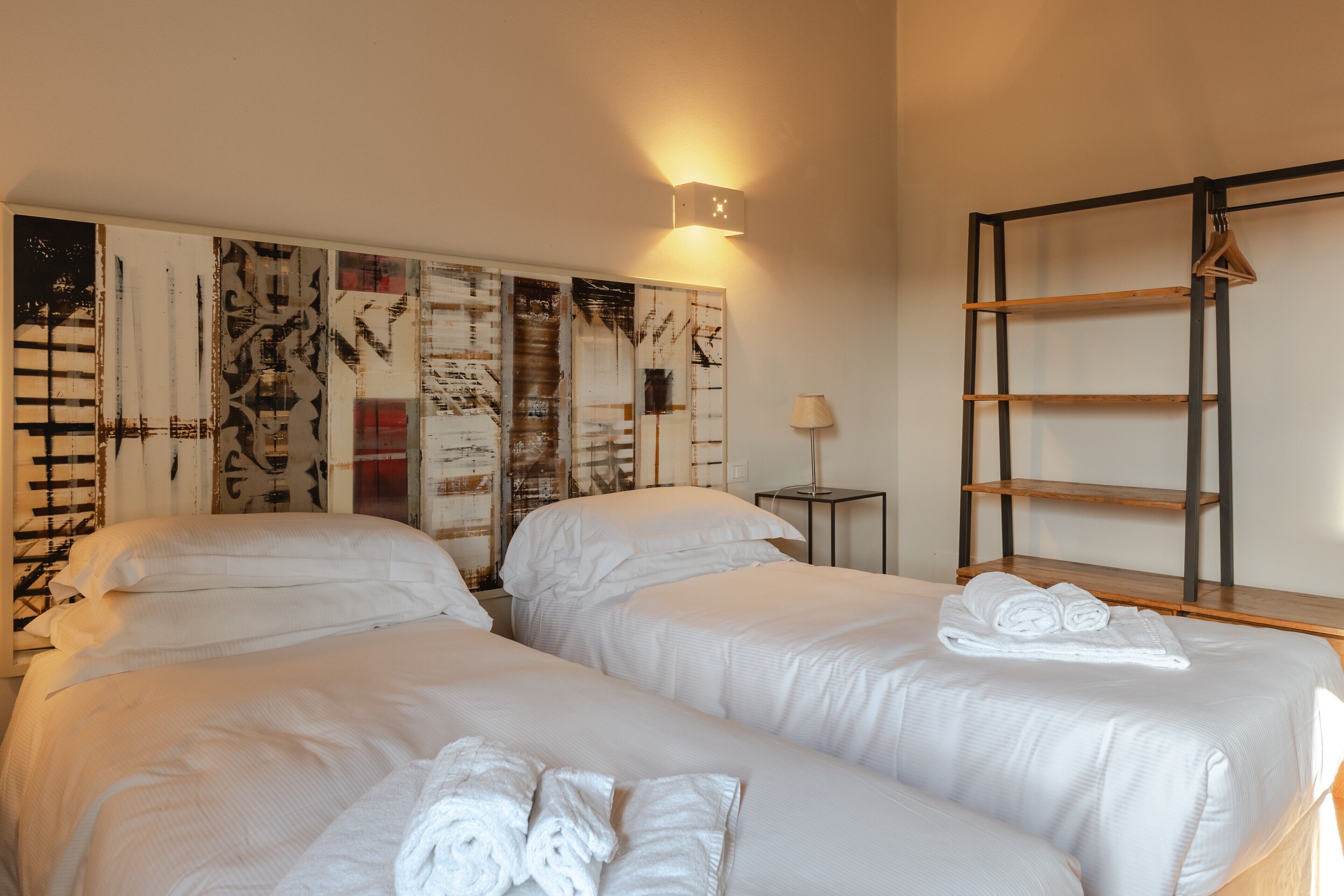 A hotel room with two beds, a wall-mounted shelf, a lamp, and a ladder.
