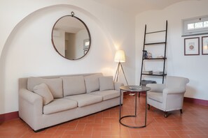 A living room with a sofa, a chair, a round table, a lamp, a mirror, a ladder, and a bookshelf. - Holiday Home 'Magazzino 1' with Shared Pool, Wi-Fi and Air Conditioning (Cortona)