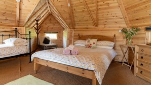 A cozy wooden cabin bedroom with two beds, a wooden dresser, and a small table with a vase of flowers. - Dartmoor Eco-Pod (Oak Tree Lane) Gorgeous rustic charm (Okehampton)