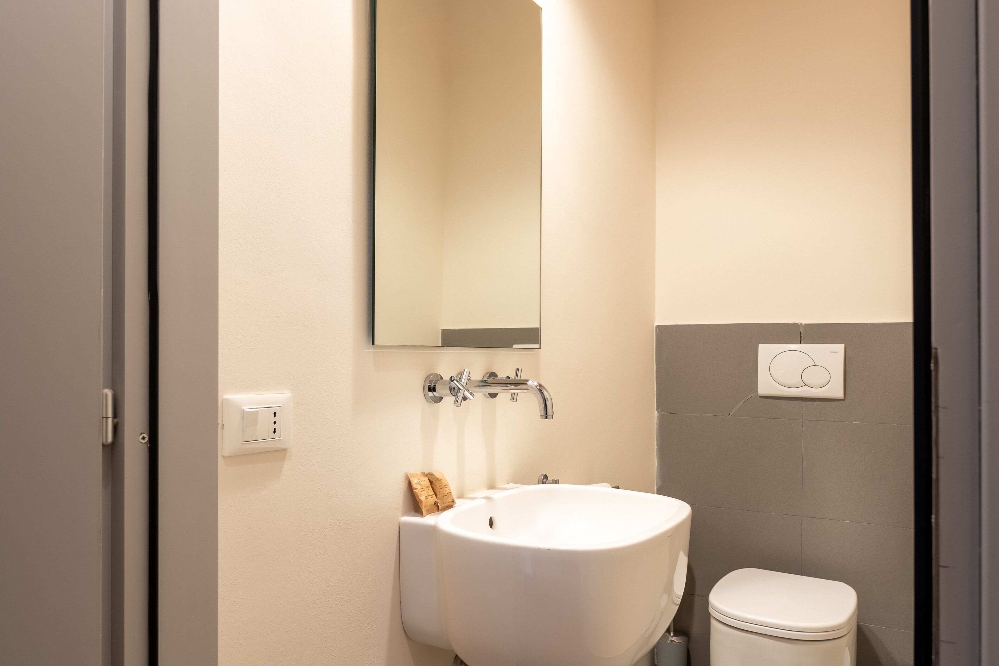 A bathroom with a white sink, a mirror, a toilet, and a light switch on the wall.