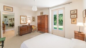 A bedroom with a bed, a wooden dresser, a chair, and a large window with a view of greenery. - ApartmentsGarda - Cottage Capre (GARDA)